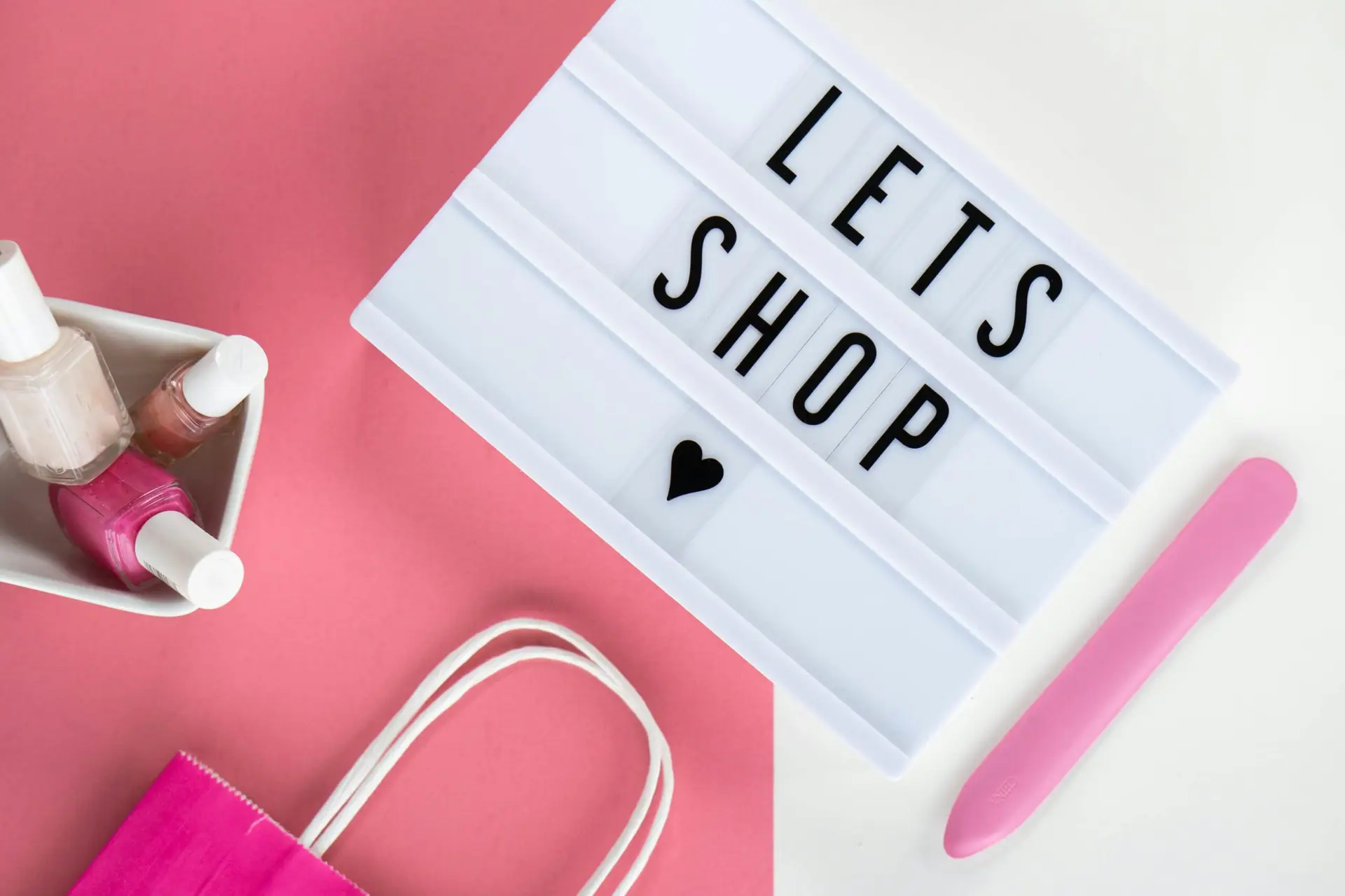 Aesthetic flat lay with a shopping theme showcasing pink accents, nail polish, and a letter board.